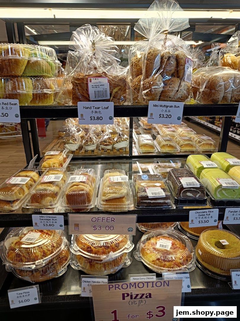 A display of various baked goods including loaves, buns, cakes, and pizzas at a FairPrice Xtra store.