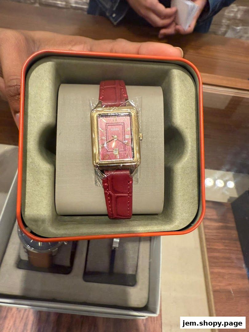 A red Fossil watch with a gold rectangular case and a red leather strap is displayed in its box.