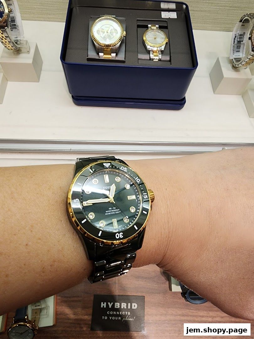 A person wearing a black and gold Fossil watch, with other watches displayed in the background.
