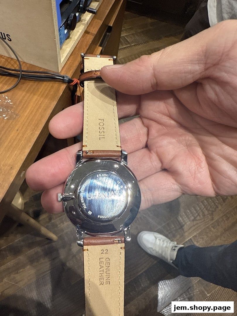 A hand holds a Fossil watch with a brown leather strap, showcasing its back.