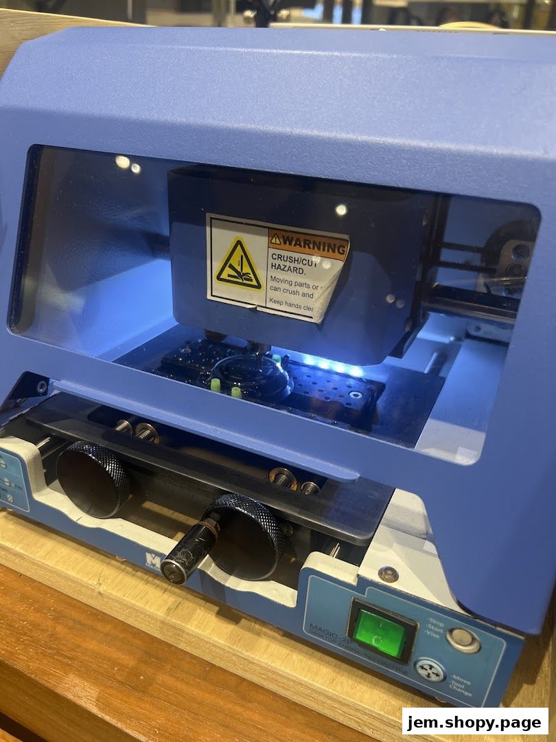 A close-up of a blue engraving machine with a warning label and operational controls.