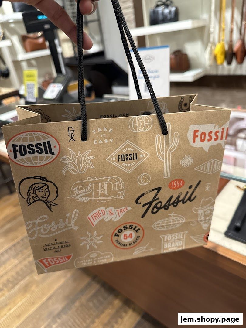 A person holds a Fossil shopping bag with various brand logos and designs.
