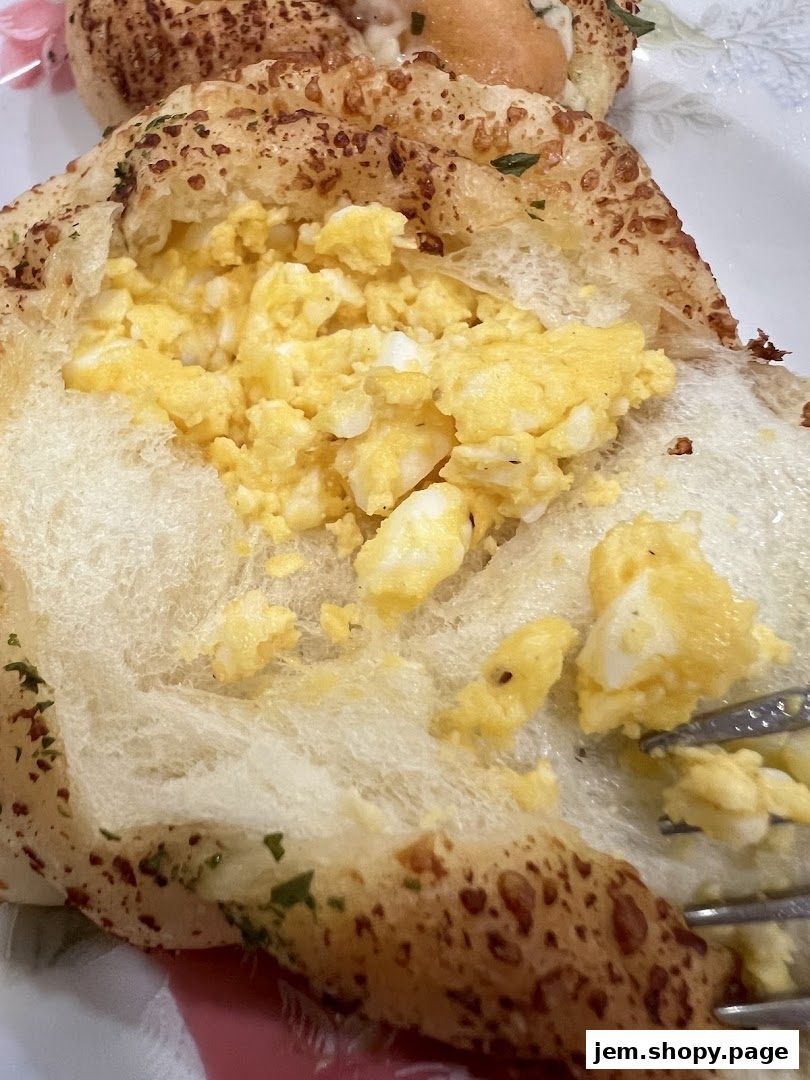 A close-up shot of a fluffy bread roll filled with scrambled eggs and herbs.