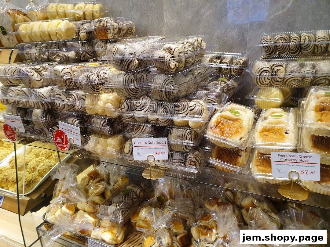 A display of various freshly baked pastries and bread rolls in clear plastic packaging.