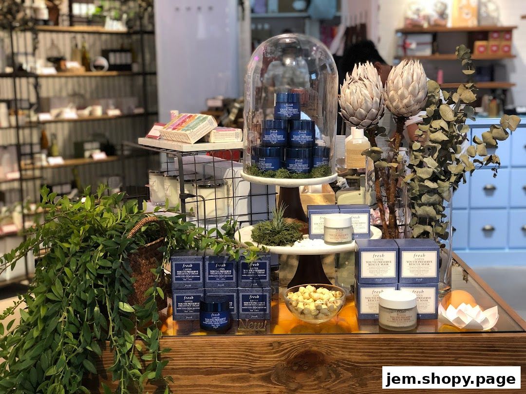 A display of Fresh skincare products, including creams and masks, with decorative plants and dried flowers.