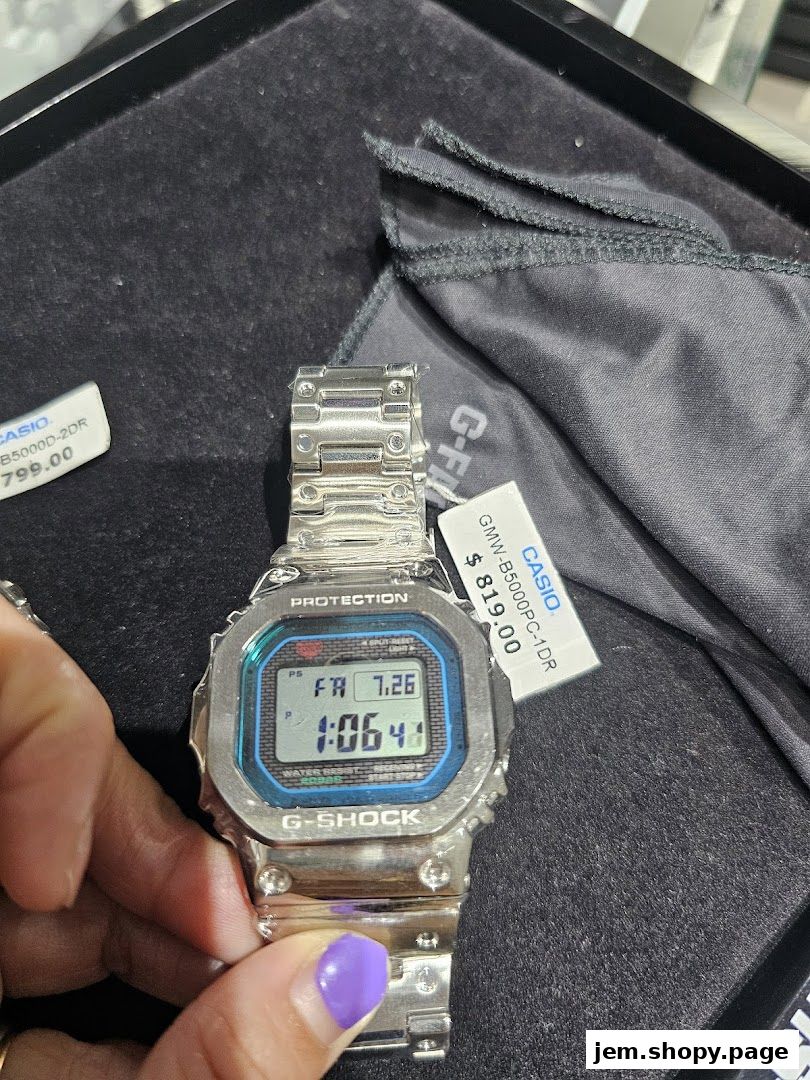 A hand holds a silver G-SHOCK watch with a blue digital display and price tags.