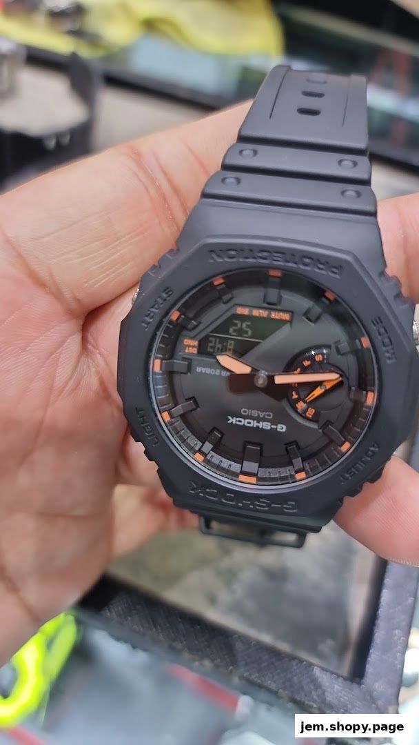 A hand holds a black G-SHOCK CASIO watch with orange accents and a digital display.