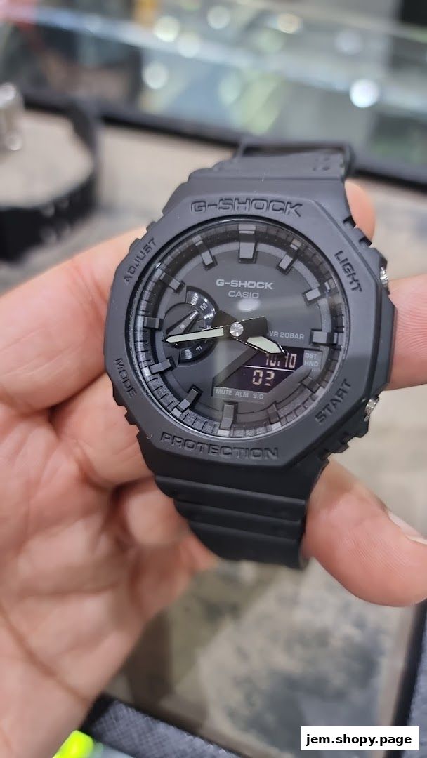 A hand holds a black G-Shock Casio watch with a digital display.