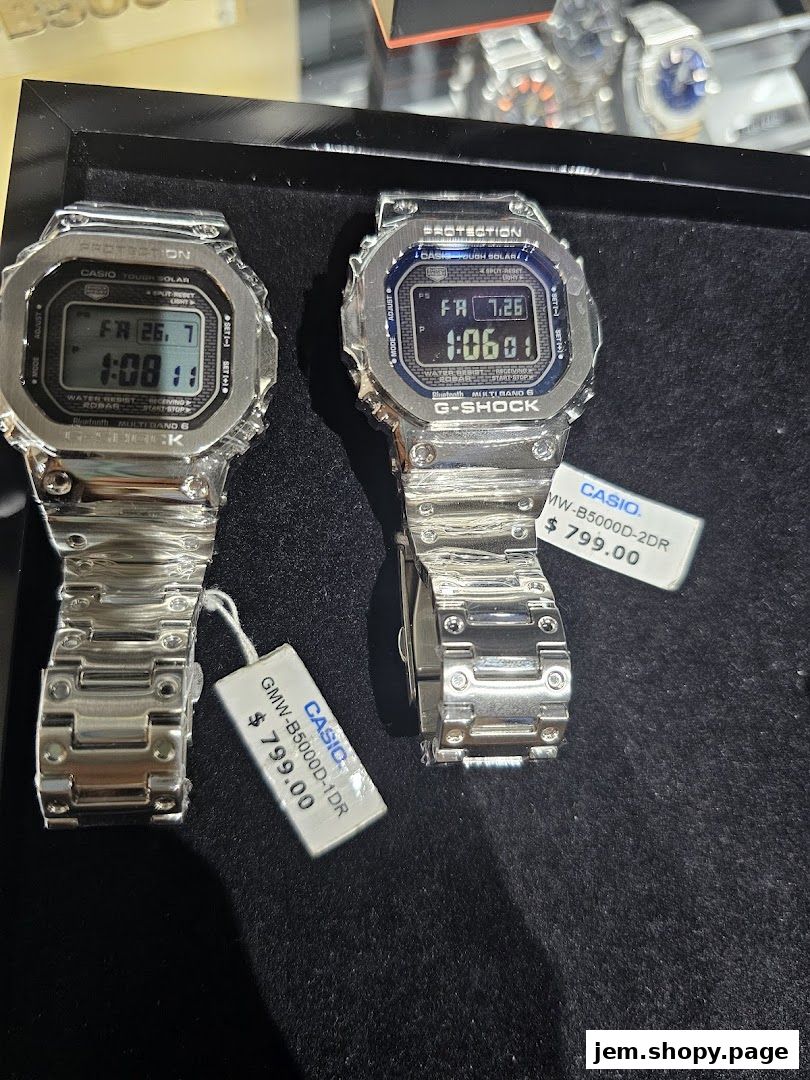 Two G-SHOCK CASIO watches with metal bands displayed on a black surface.