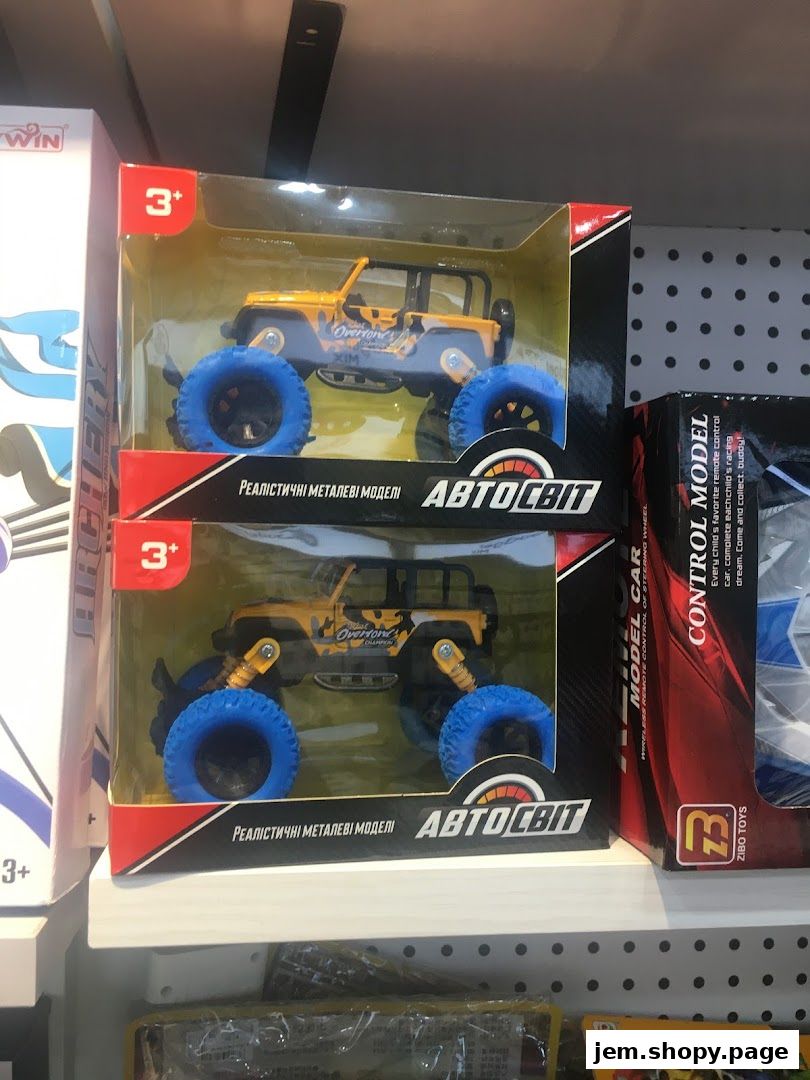 Two boxed toy monster trucks with large blue wheels are displayed on a shelf.