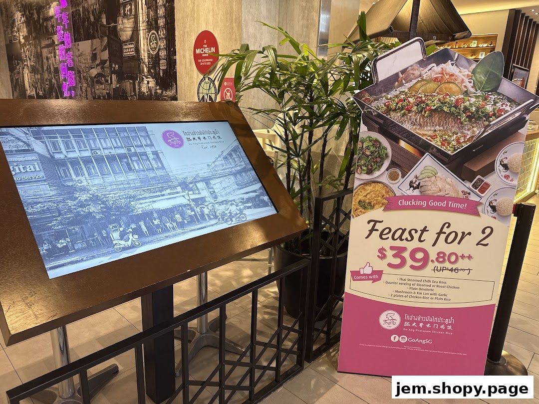 A digital display and a promotional sign for a chicken rice restaurant.