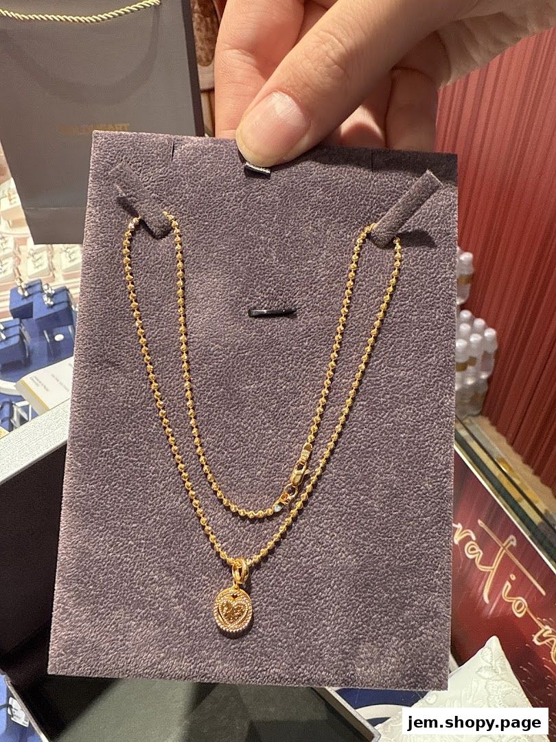 A hand holds a gold necklace with a heart-shaped pendant on a display card.