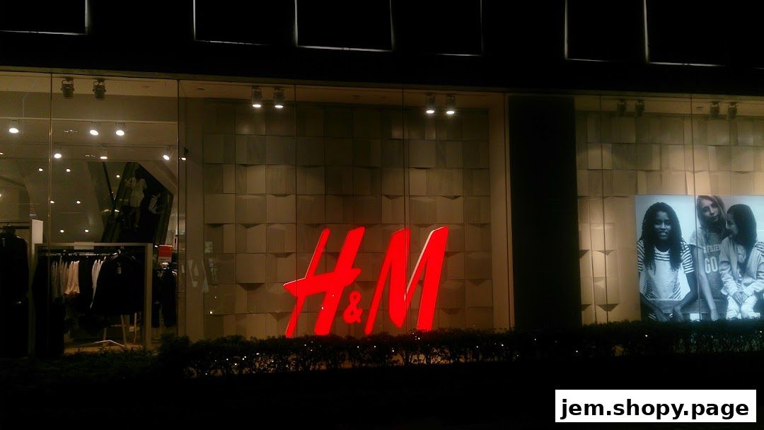 The H&M store front at night, featuring a large illuminated logo and window displays.