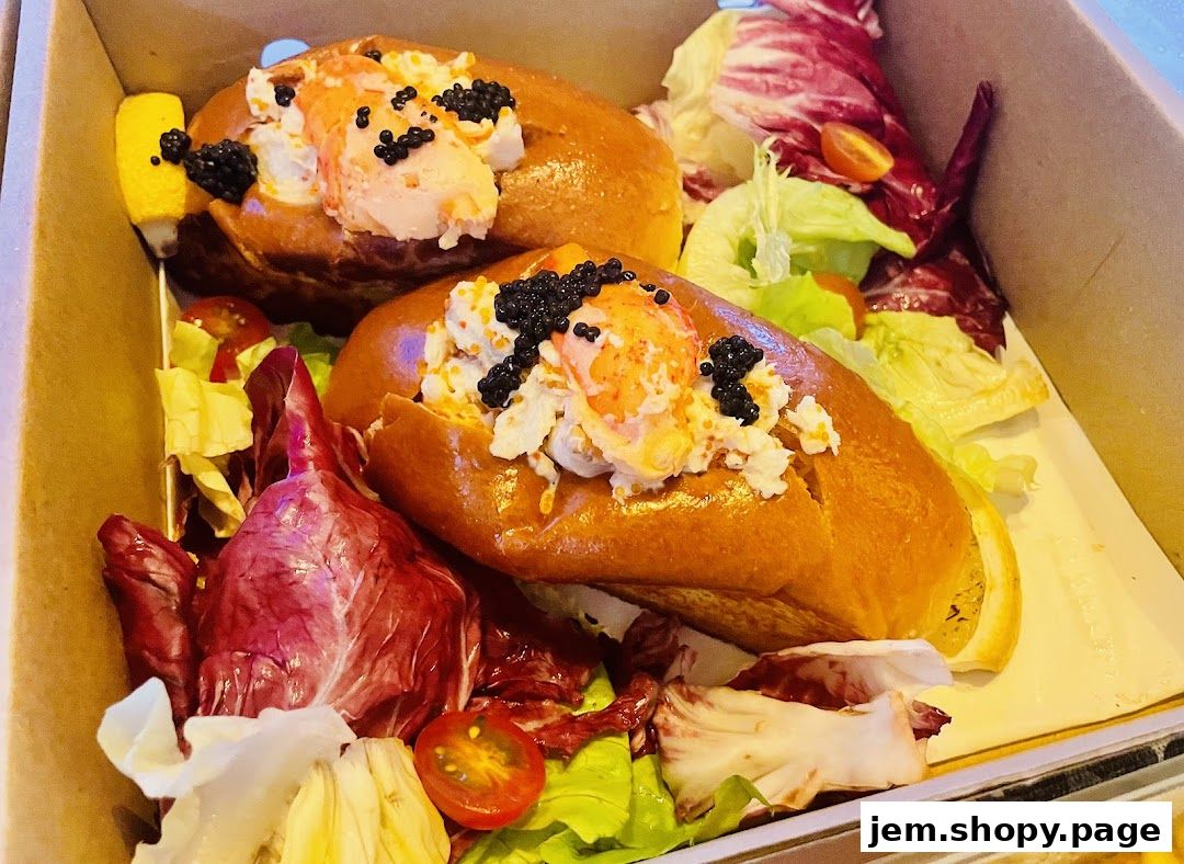 Two gourmet lobster rolls with caviar and a side salad in a takeout box.