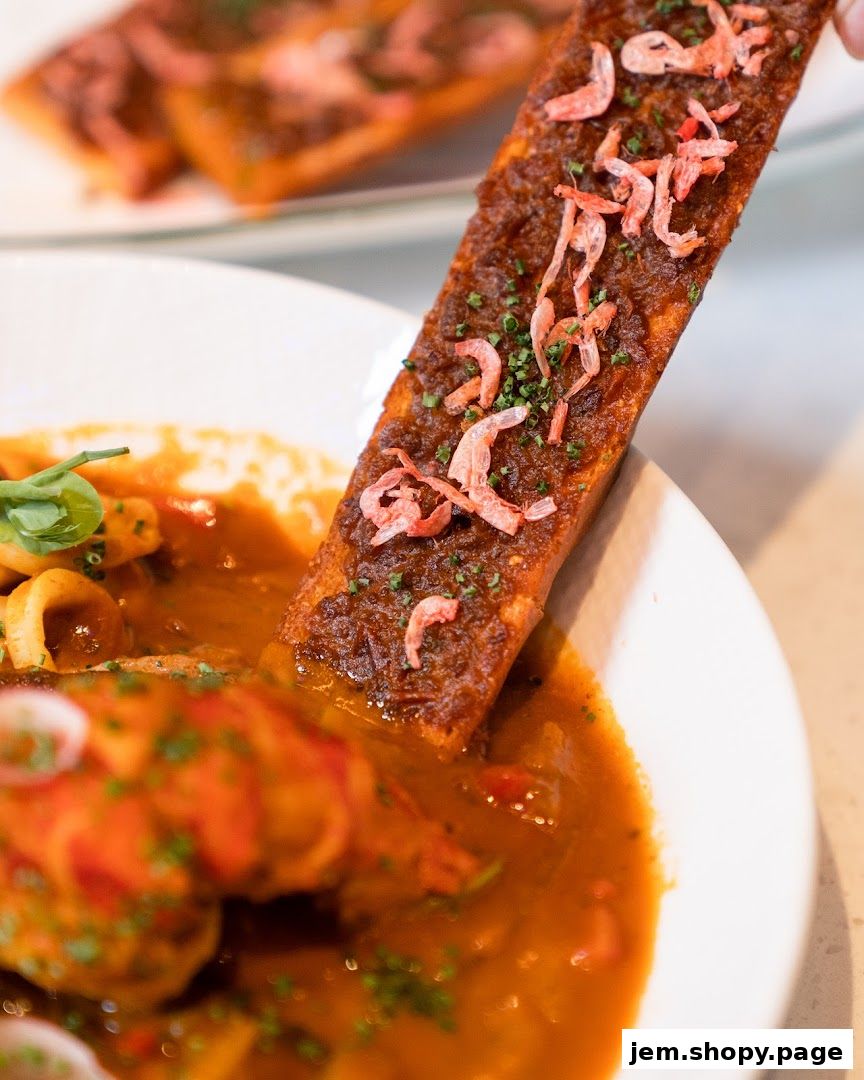A close-up of a piece of toast with shrimp and sauce, dipped into a bowl of stew.