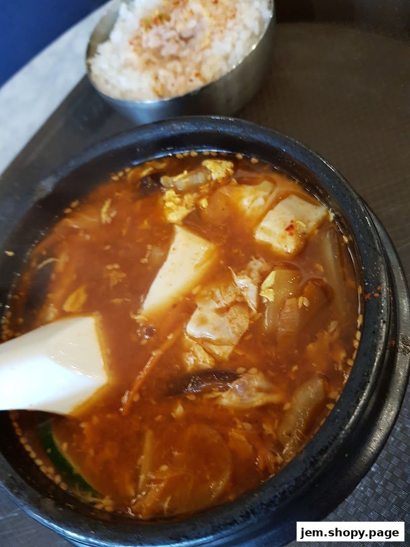 A close-up of a steaming bowl of Korean stew with tofu and a side of rice.