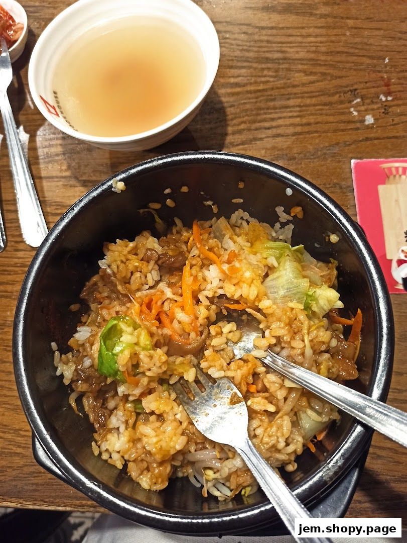 A close-up of a Korean dish with rice, meat, and vegetables, served with a side of broth.