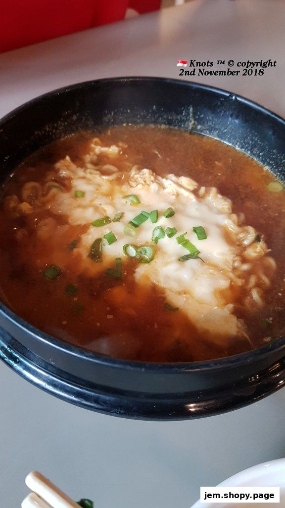 A steaming bowl of Korean ramen topped with melted cheese and green onions.