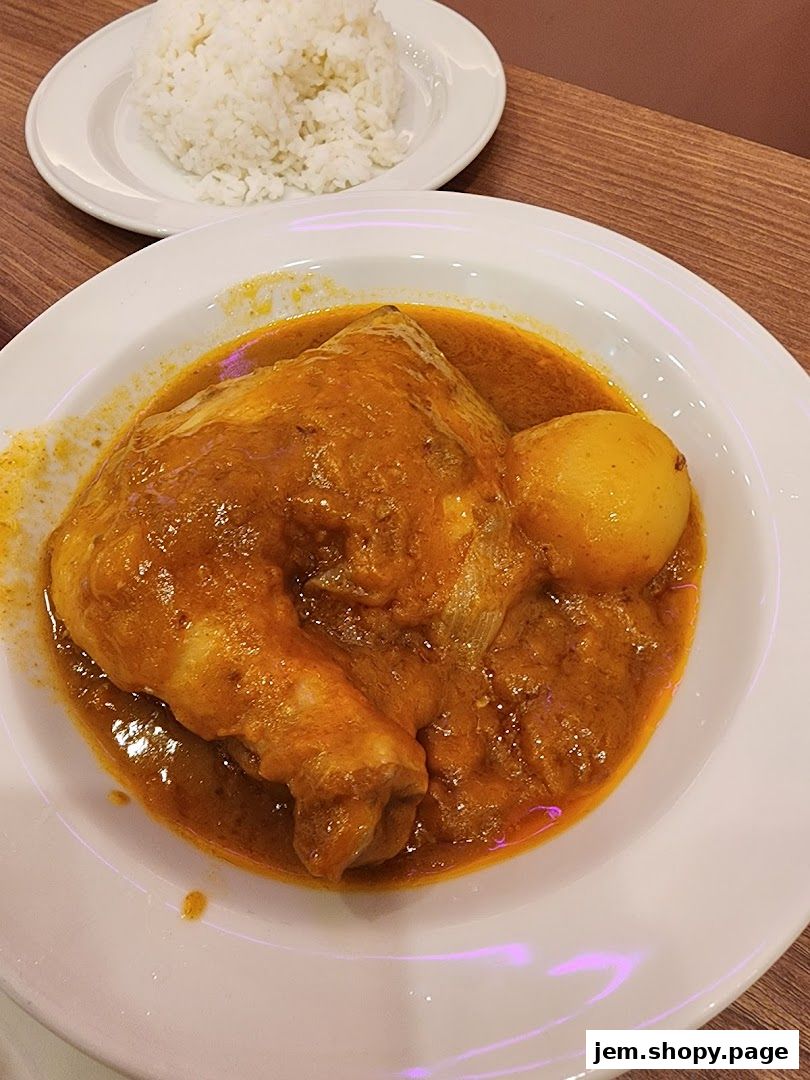 A plate of chicken curry with potatoes and a side of white rice.