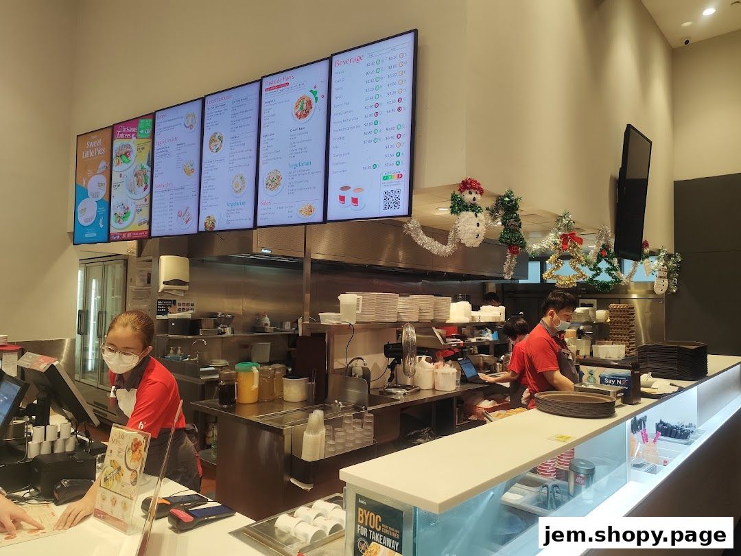 Digital menus display food and drink options above a food service counter with staff.