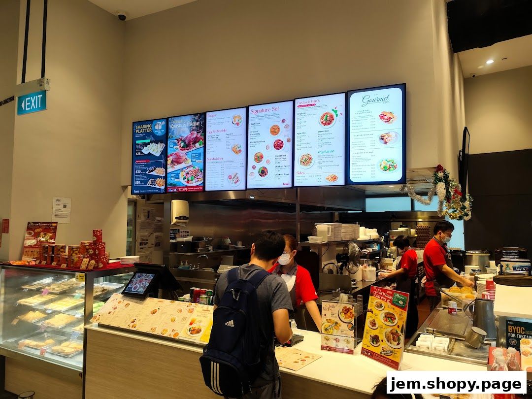 Digital menus display food options and prices at a restaurant counter with staff preparing orders.