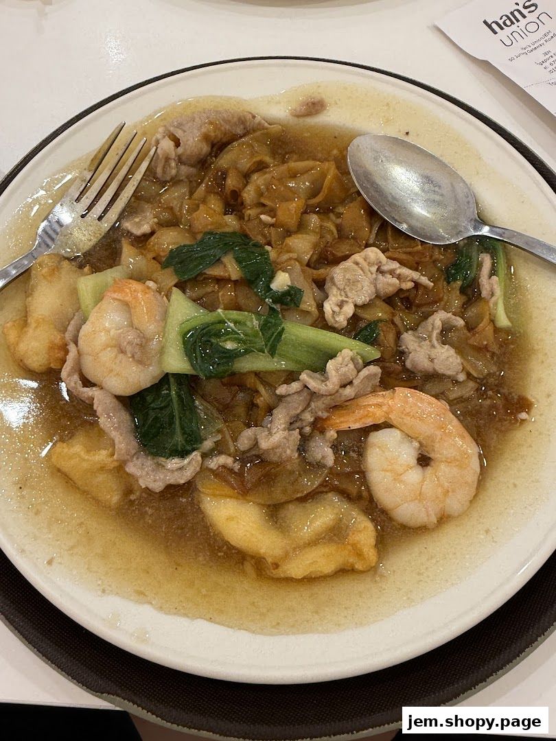 A plate of delicious hor fun with prawns, pork, and vegetables, served with a fork and spoon.