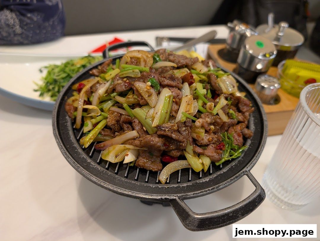 A sizzling hot plate of stir-fried beef with vegetables and a side dish.