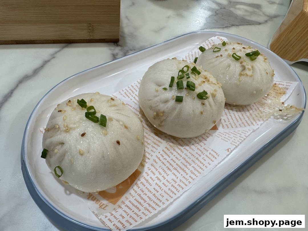 Three steamed buns topped with sesame seeds and chopped green onions on a platter.