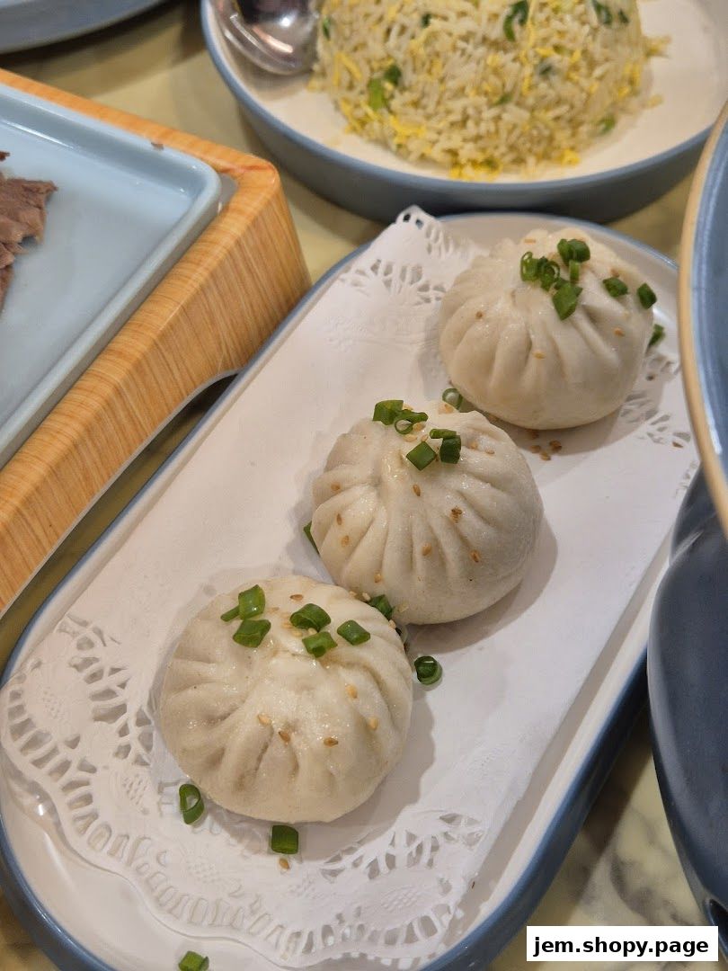 Three steamed buns topped with sesame seeds and green onions on a white plate.