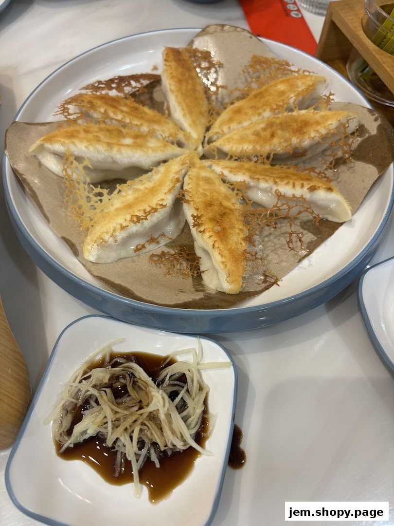 A plate of golden-brown pan-fried dumplings served with a side of shredded ginger and soy sauce.
