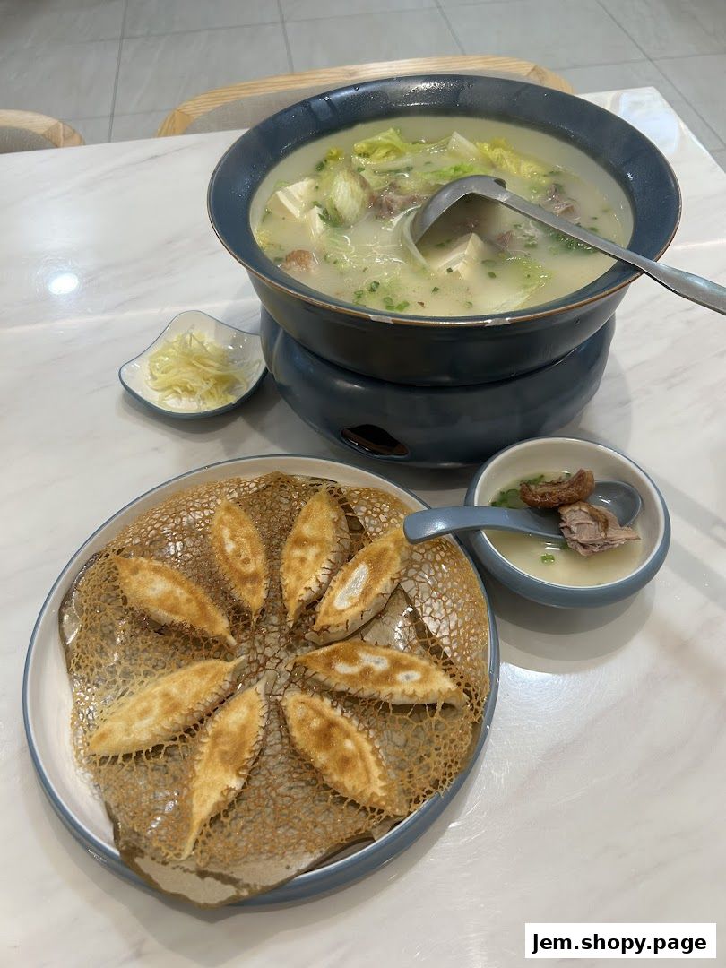 A steaming pot of soup with tofu and vegetables, served with pan-fried dumplings and a side of ginger.