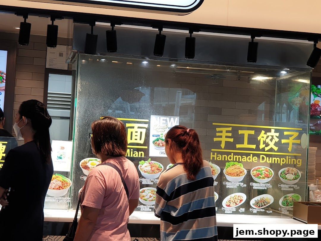 People looking at a display of noodle and dumpling dishes at a food stall.