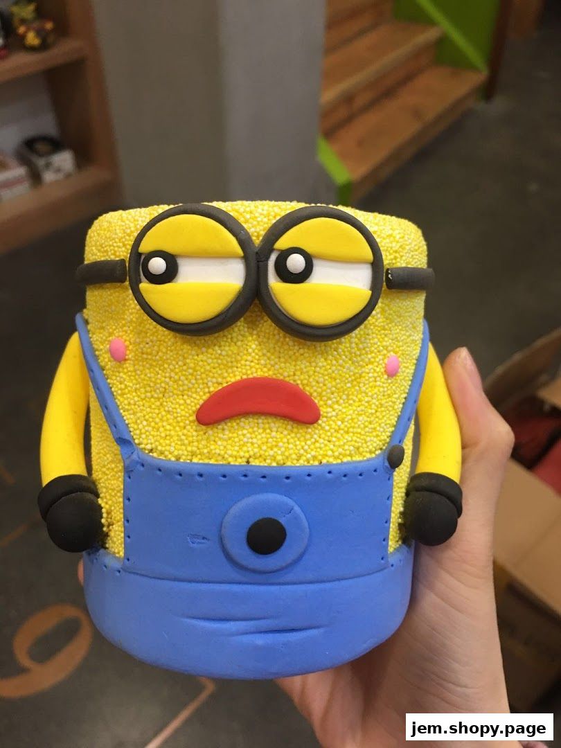 A hand holds a Minion-themed cake decorated with yellow sprinkles and blue overalls.
