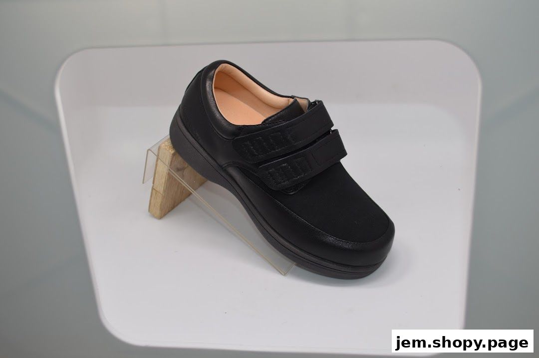A black shoe with velcro straps is displayed on a white stand.