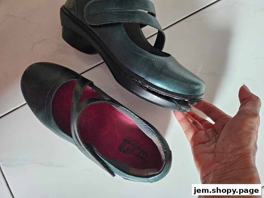 A hand points to a damaged sole on a pair of teal Mary Jane shoes.