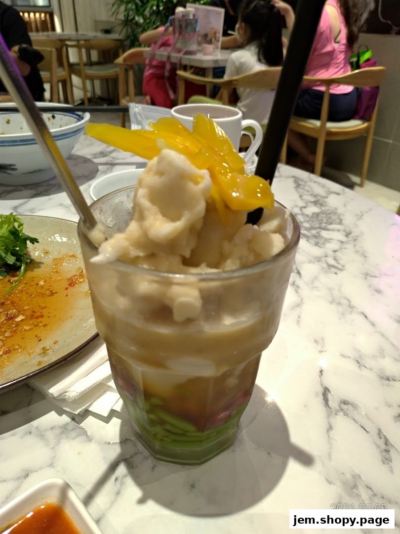 A refreshing dessert with shaved ice, mango, and jelly layers, served in a glass.