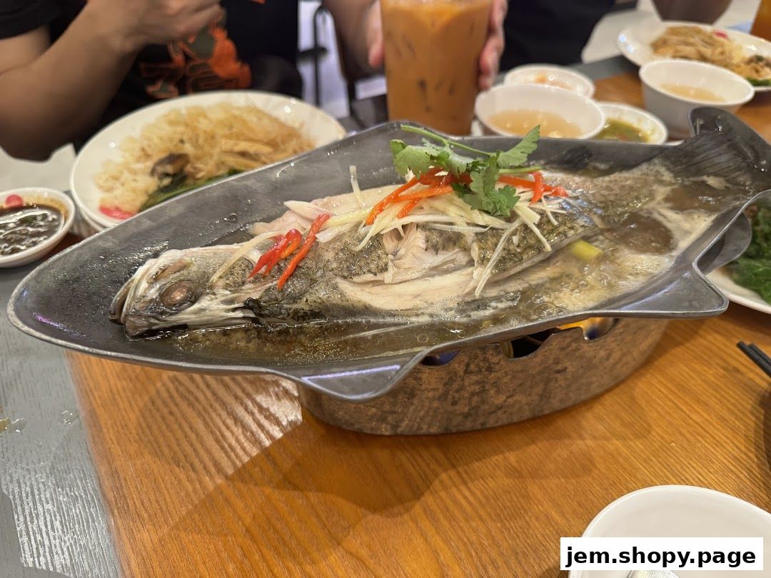 A whole steamed fish dish served with ginger, chili, and herbs on a warming plate.