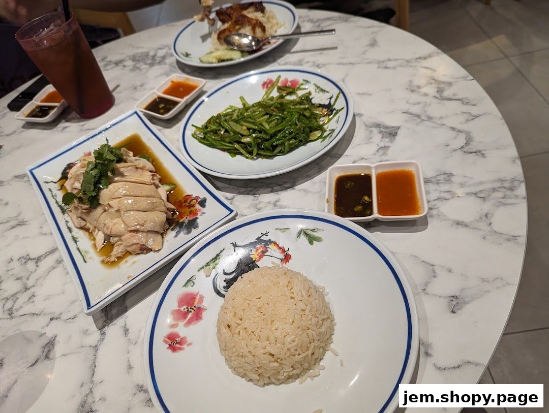 A table laden with delicious chicken rice, vegetables, and dipping sauces.