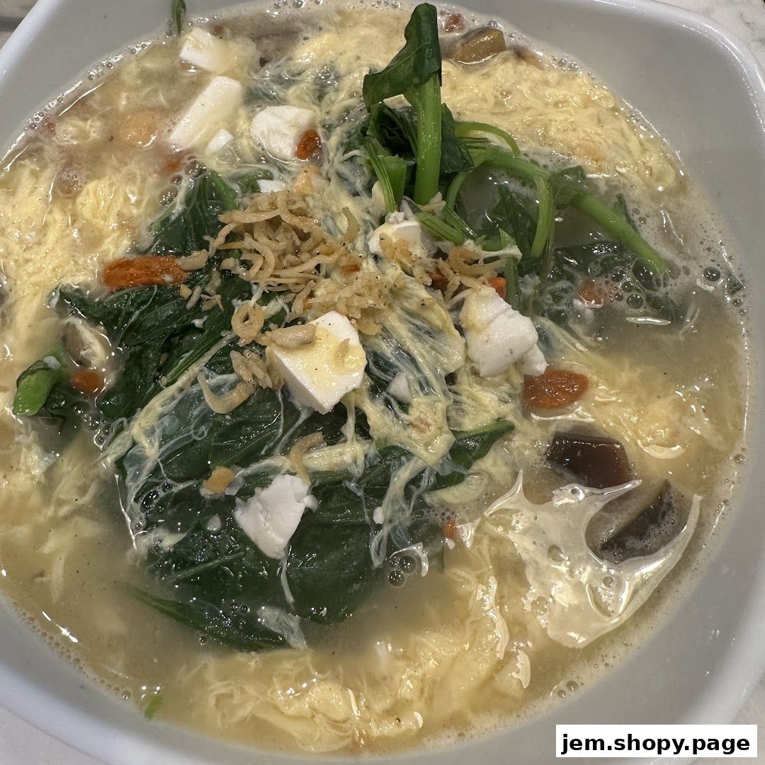 A close-up of a steaming bowl of soup with vegetables, tofu, and egg.