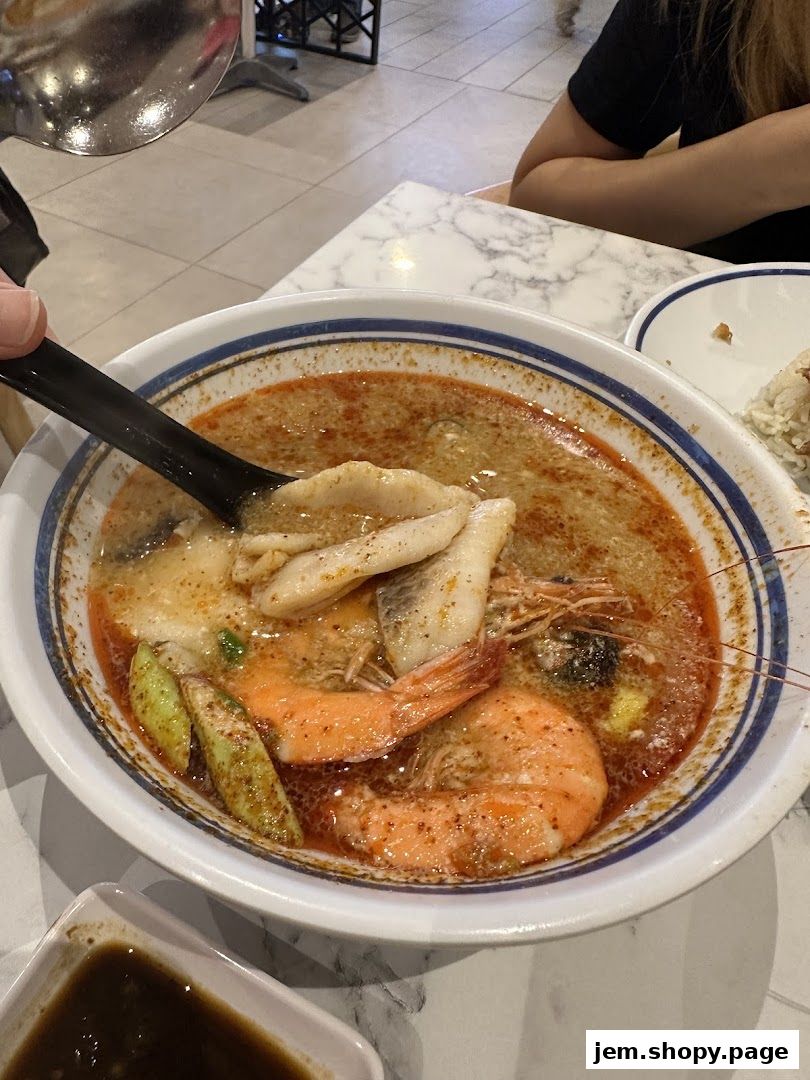 A close-up of a steaming bowl of seafood soup with shrimp and fish.