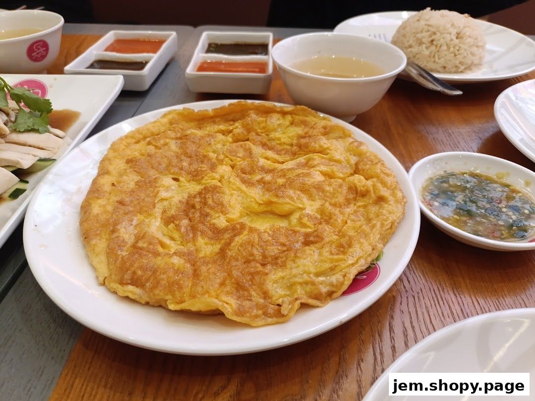 A close-up of a fluffy omelet served with chicken rice and dipping sauces.