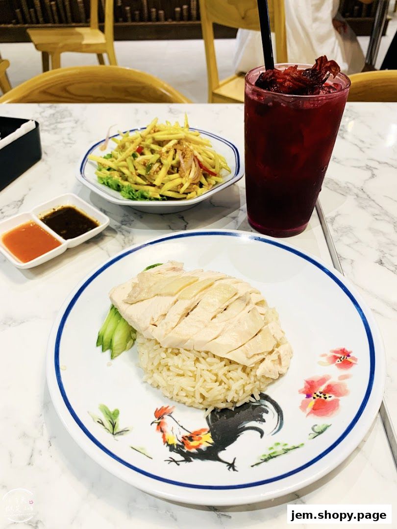 A plate of Hainanese chicken rice with a side of mango salad and a red drink.