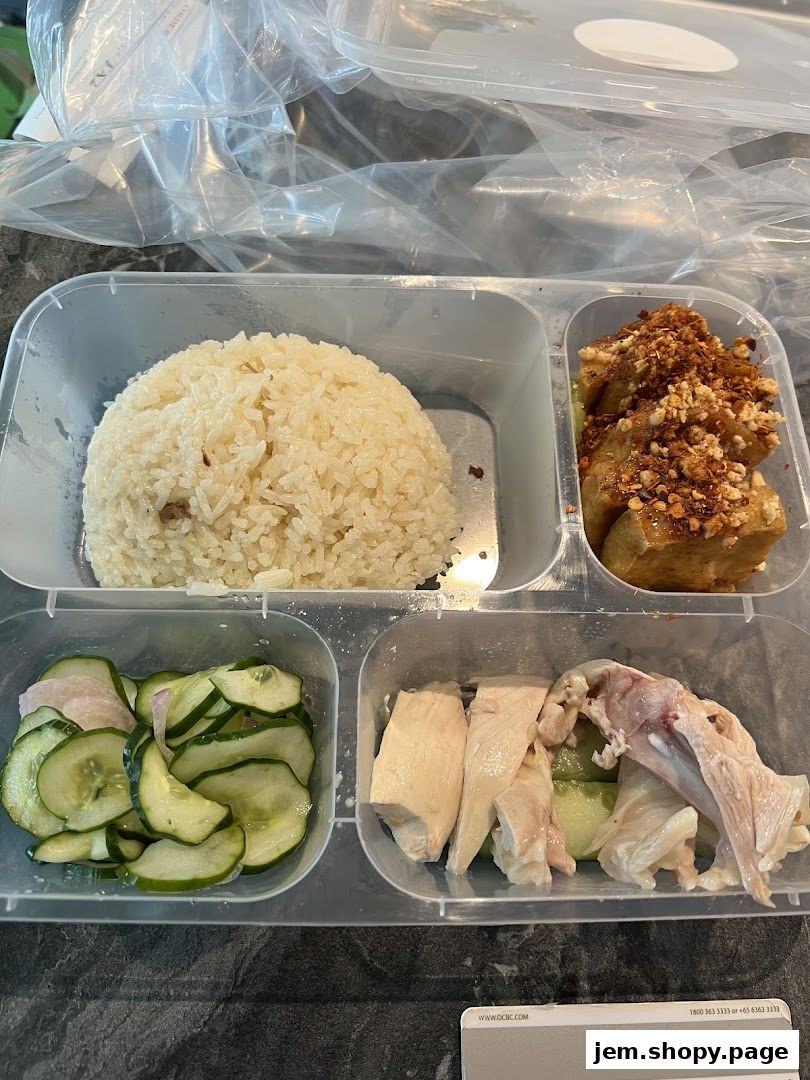 A takeaway container filled with chicken rice, cucumber slices, and fried tofu.