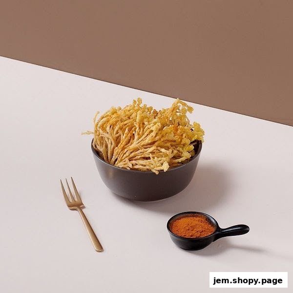 A bowl of crispy fried enoki mushrooms with a side of chili powder and a fork.