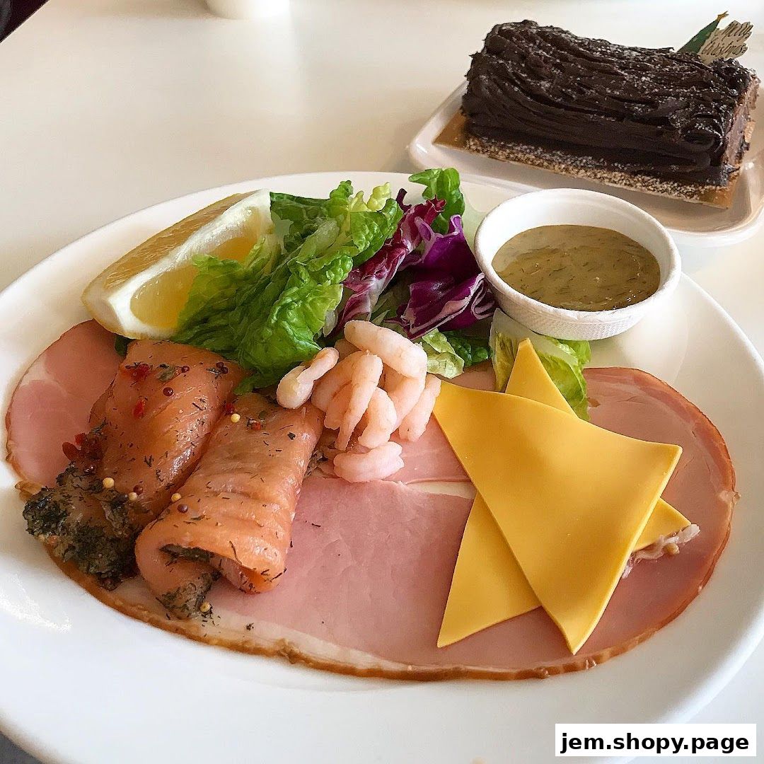 A plate of smoked salmon, ham, cheese, shrimp, salad, and a slice of chocolate cake.