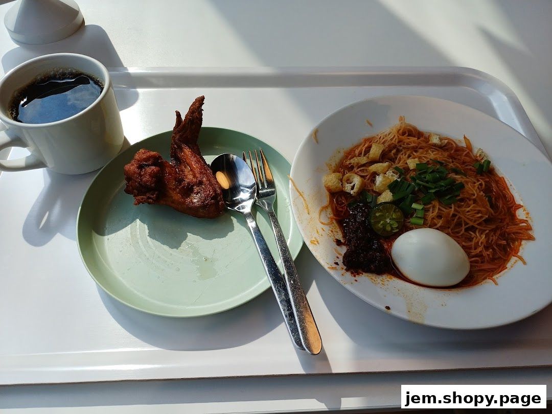 A tray with a meal including noodles, fried chicken wing, boiled egg, and coffee.