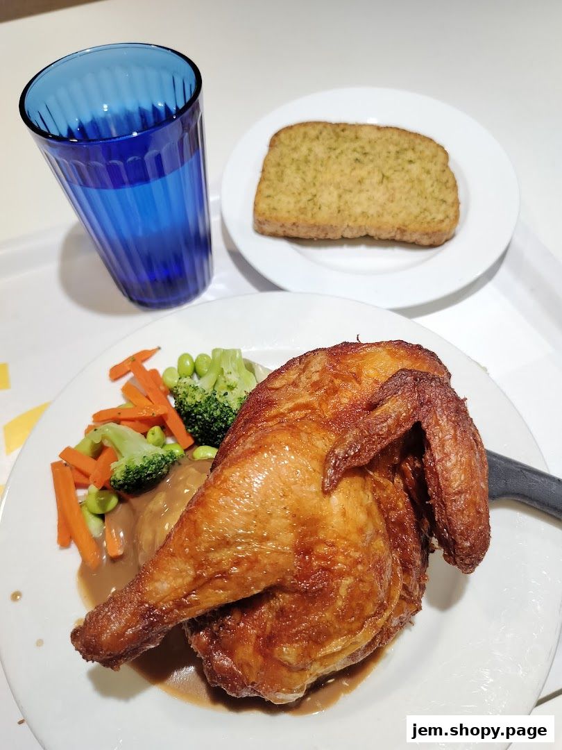 A plate of roasted chicken with vegetables, gravy, and a slice of garlic bread, served with a blue glass of water.