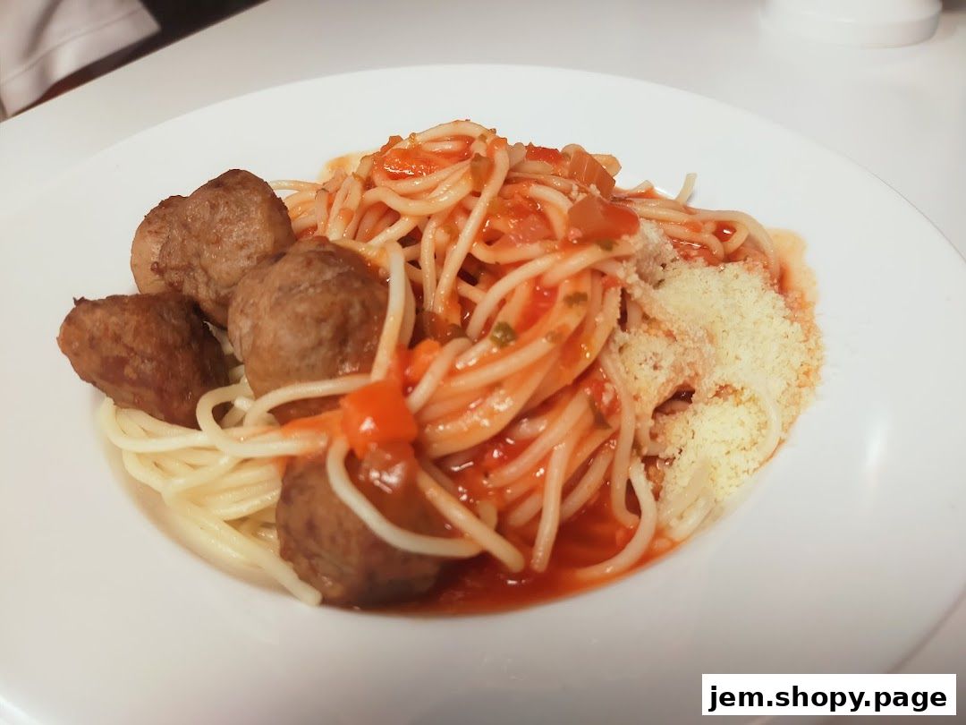 A plate of spaghetti with meatballs and tomato sauce, topped with grated cheese.
