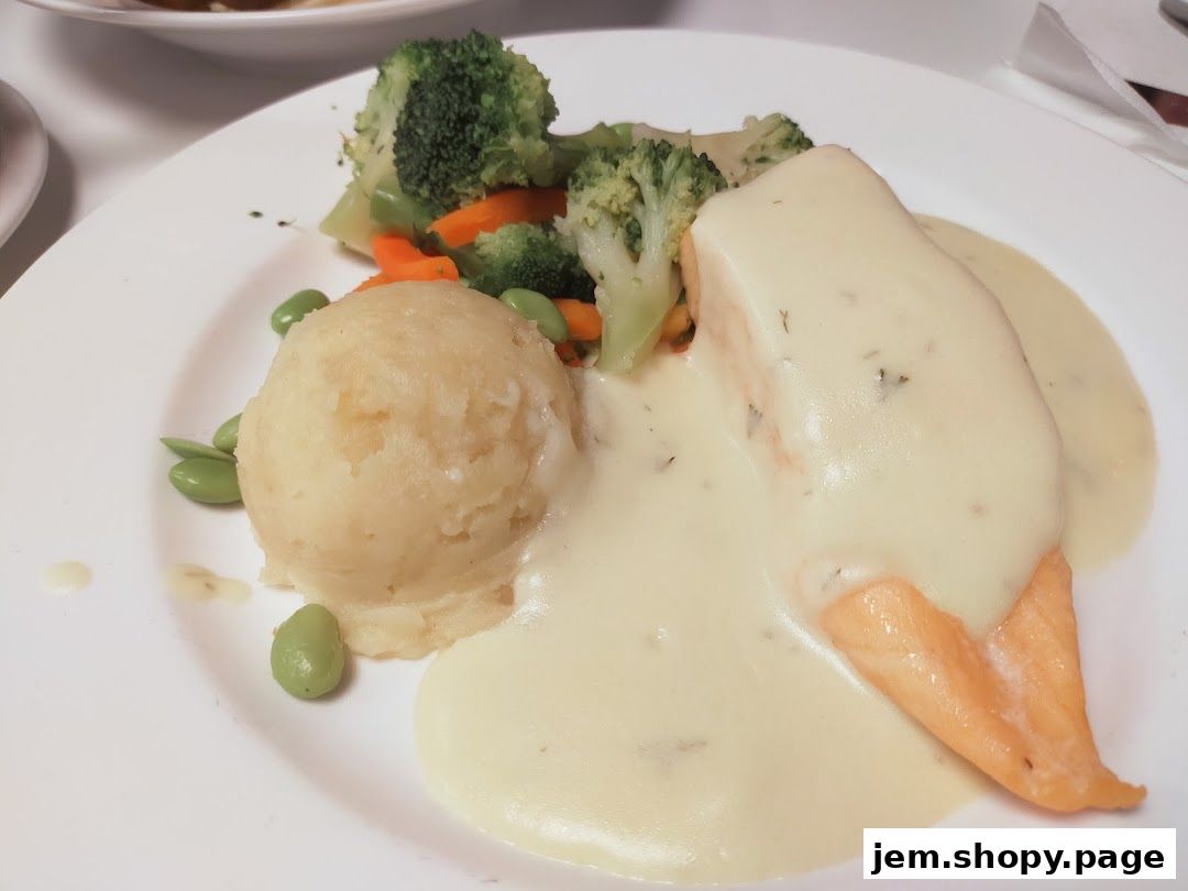 A plate of salmon with mashed potatoes and steamed vegetables, covered in a creamy sauce.