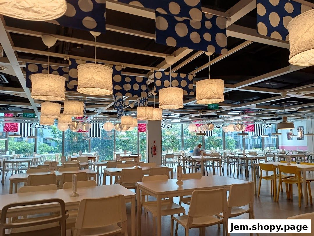 Interior of a spacious IKEA restaurant with many tables and chairs, illuminated by decorative lamps.